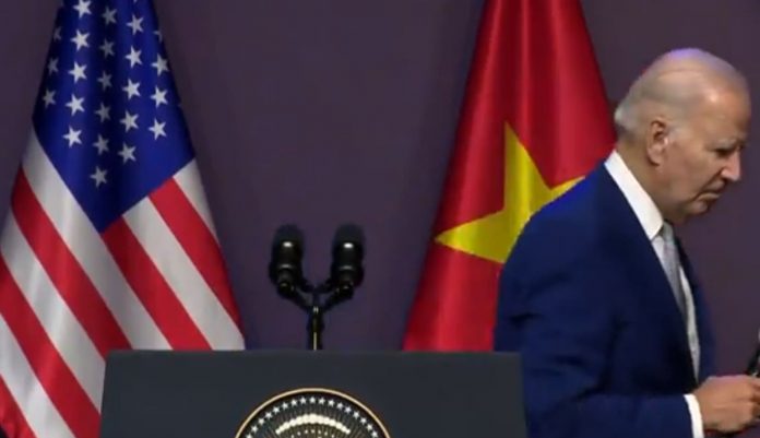 old-joe-biden-gets-distracted,-bends-down-to-fiddle-with-something,-then-walks-out-of-camera-frame-while-he-is-being-asked-a-question-in-vietnam